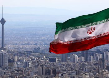 Iran's national flag waves as Milad telecommunications tower and buildings are seen in Tehran, Iran, Tuesday, March 31, 2020. In recent days, Iran which is battling the worst new coronavirus outbreak in the region, has ordered the closure of nonessential businesses and banned intercity travels aimed at preventing the virus' spread.   (AP Photo/Vahid Salemi)